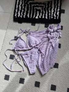 Three-piece lavender bikini set featuring ruffle textures and a matching beach sarong
