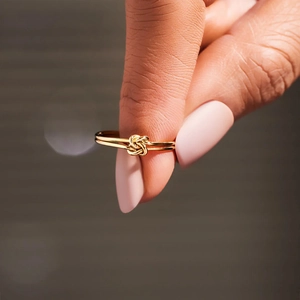 Close-up of golden double-layer knot ring on finger with dark blurred background
