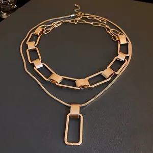 Chic layered gold chain necklace featuring a rectangular pendant on a matte dark base