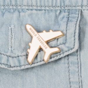 Detail of 3D airplane brooch with white enamel and WORLD TRAVELER text on denim
