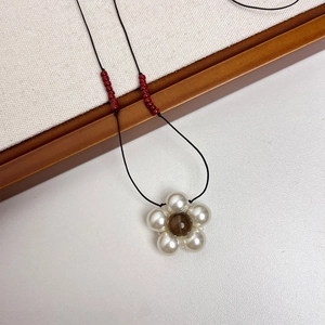 Detail of floral pearl pendant on black cord with red bead accents for a vintage look