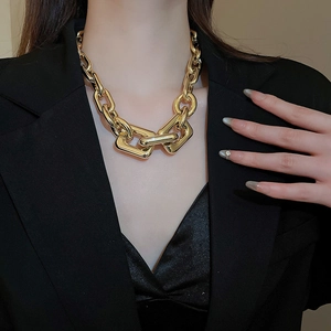 Close-up of chunky gold chain necklace with polished rectangular links on black blazer