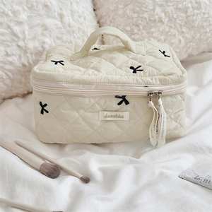 Close-up of quilted cosmetic bag with black bow embroidery and beige ribbon zipper puller