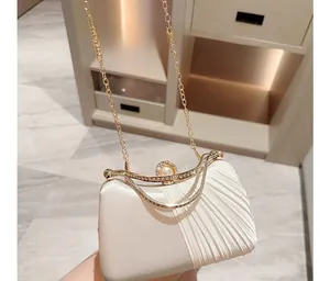 Detail of elegant ivory satin clutch bag with pearl clasp and gold chain strap