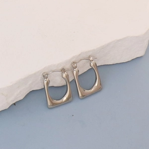Detailed macro view of silver geometric hoop earrings on a white textured stone background