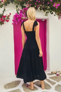 Back view of a black tiered backless dress with tie-up straps in a lush floral setting