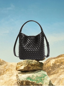 Detail of hand-woven black leather bucket bag on rocks against a clear blue sky