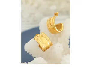 Close-up of golden C-shaped earrings with textured wavy surface on a white coral stand