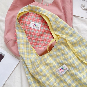 Flat lay of plaid and solid fabric tote bags with colorful logo tags on white linen