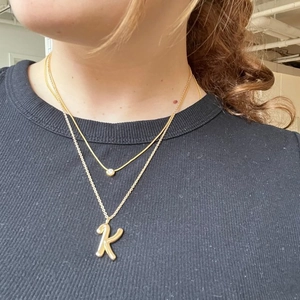 Close-up of layered 18K gold letter K pendant necklace and sparkly stone choker
