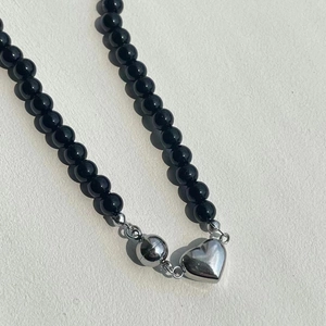 Close-up of black beaded necklace with silver heart pendant and magnetic clasp closure
