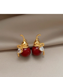 Macro shot of gold-plated red gourd earrings with zircon hearts on satin cloth