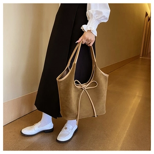 Brown suede tote bag with stylish bow tassels carried by model in indoor street style