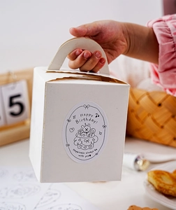 Close-up of hand holding a white paper gift box with a Happy Birthday bear sticker