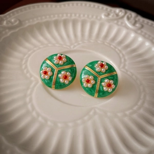 Vintage green enamel flower earrings with pearls and gold trim on white ceramic plate