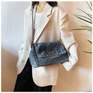 Detail of vintage denim crossbody bag with metal chain strap worn by a model in a beige suit