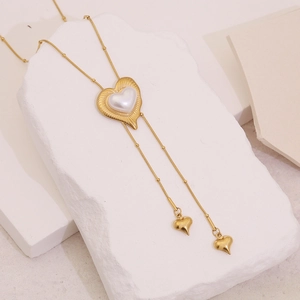 Elegant gold heart pendant necklace with pearl inlay and long tassel on stone background