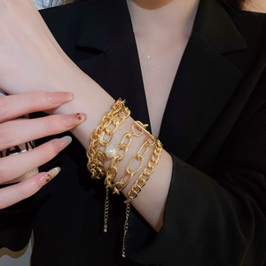 Detail of gold chain bracelet set with white pearl accents on black suit background
