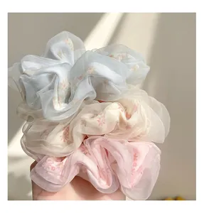 Dettaglio di tre elastici in organza con stampe floreali nei colori blu, beige e rosa