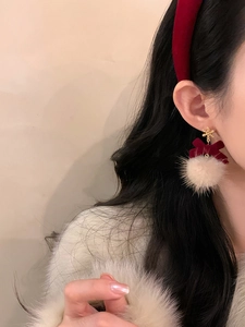Close-up of festive red velvet bow and white plush ball earrings on model ear