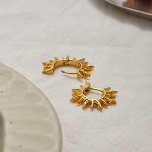 Detailed view of textured sunburst 18K gold plated stainless steel hoop earrings on linen