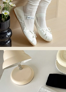 Close-up of white ballerina flats with bow detail and striped knit mid-calf socks