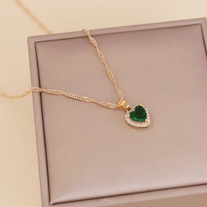 Golden heart necklace with emerald zircon and diamond halo on beige jewelry box