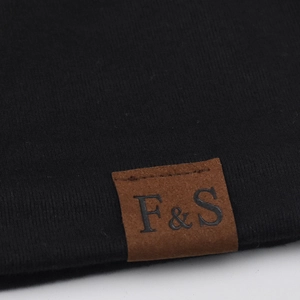 Detail of the F&S leather label stitched on a black breathable cotton knit beanie