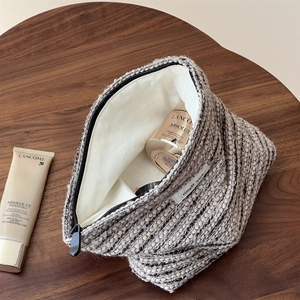 Textured tweed toiletry bag with zipper and inner lining on a wooden background