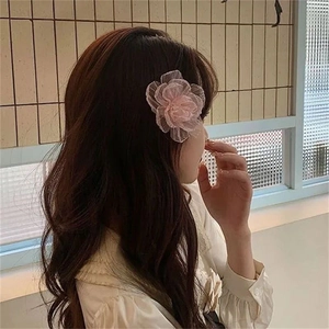 Pink fabric camellia hair clip with mesh detail worn on the side of woman's hair