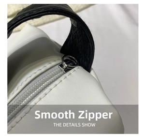 Close-up of smooth silver zipper and black woven handle on white leather handbag