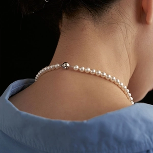 Elegant white pearl necklace with silver spherical clasp shown on model neck