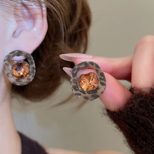 Detail of round leopard print earring with an amber crystal stone and textured fabric