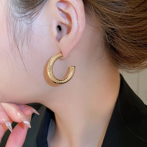 Macro side view of gold C-shaped earrings with hammered texture on female model