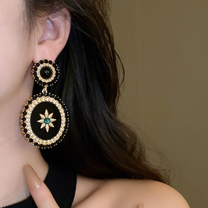 Detail view of retro baroque oval earrings with black resin and golden starburst pattern