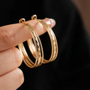 Large gold round earrings with diamond texture shown held by hand for scale