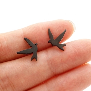 Minimalist black swallow bird stud earrings in matte finish shown on finger