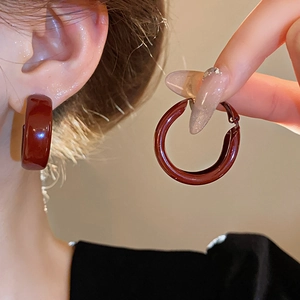 Detail view of dark red enamel C-shaped hoop earrings worn on model and held in hand