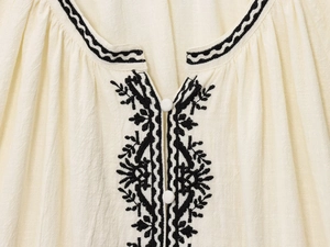 Close-up of ethnic floral embroidery and button detail on a beige cotton-linen shirt