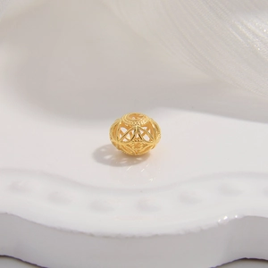 Golden S925 silver hollow spacer bead with geometric cutouts on white ceramic plate