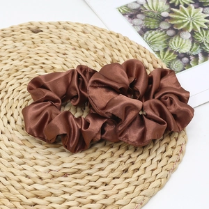 Detail view of two glossy brown satin silk hair scrunchies on a woven straw mat