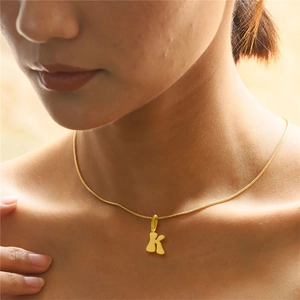 Close-up of a delicate gold letter K pendant necklace worn on a woman's neck