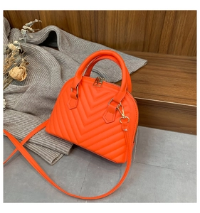 Detail of bright orange shell bag with V-shaped quilting and gold zipper hardware