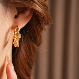 Detailed view of leaf-shaped gold-plated hoop earrings worn by a model in close-up