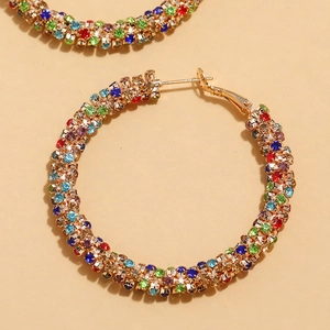 Macro view of oversized gold hoop earrings with multi-colored crystals on yellow background