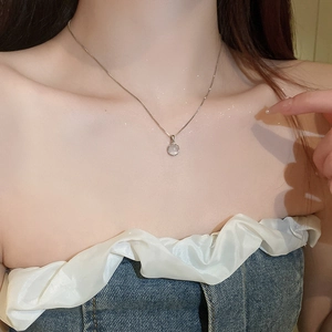 Close-up of minimalist silver necklace with round cat-eye stone worn on collarbone
