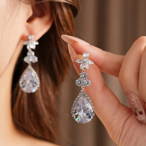 Detailed view of teardrop zircon earring with flower motif on model's ear