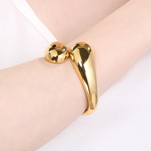 Detailed close-up of a polished gold irregular cross open bangle worn on a model wrist