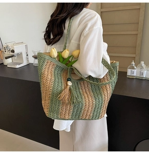 Detailed close-up of woven straw tote bag with green stripes and decorative tassel fringe