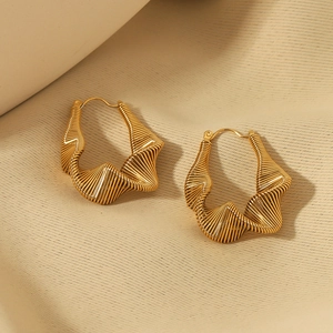 Détail macro de boucles d'oreilles torsadées dorées avec motif fileté sur un tissu doux